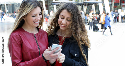 Two happy women friends looking at a smartphone outdoor