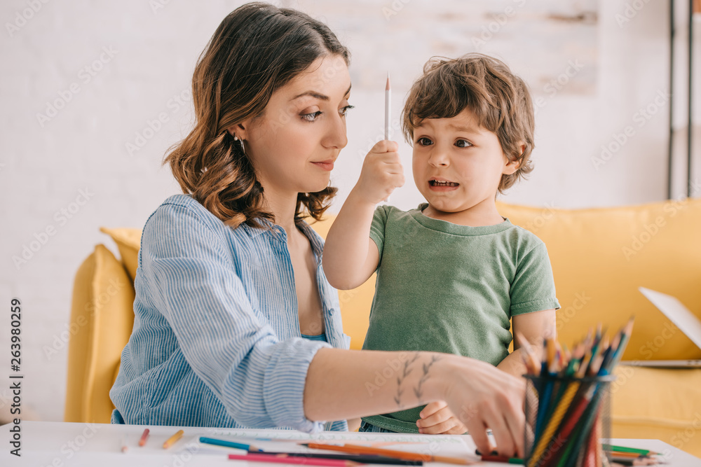 amazed kid holding color pencil while drawing with mom amazed kid holding color pencil while drawing with mom