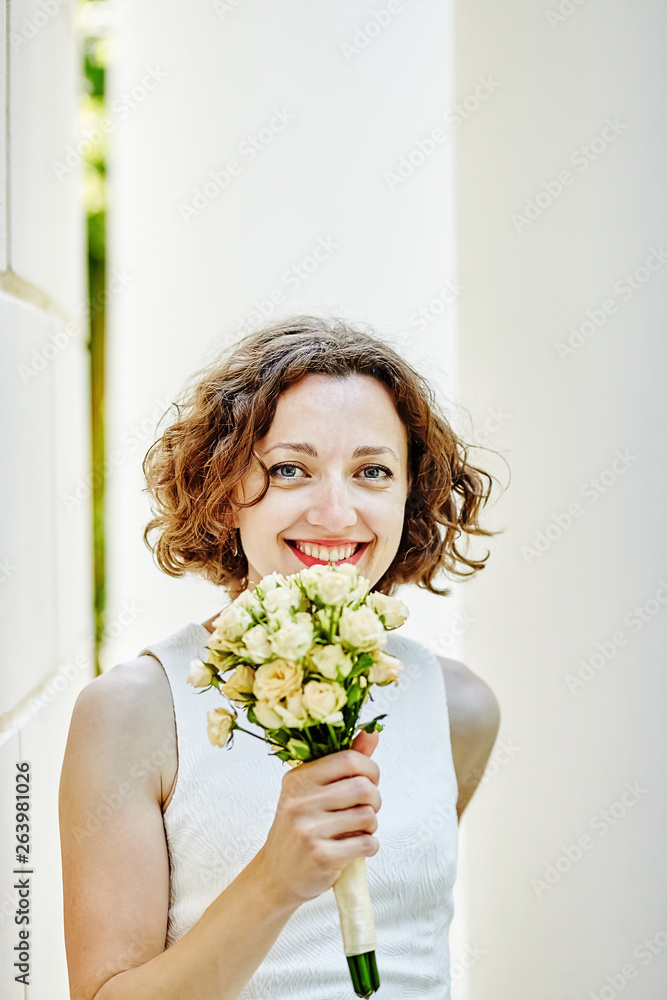 Portrait of smiling young woman with red lipstick in white dress outdoor. Curly brown hair bride with a wedding bouquet Portrait of smiling young woman with red lipstick in white dress outdoor. Curly brown hair bride with a wedding bouquet