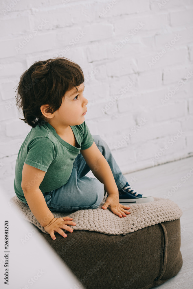 Obraz premium Child in green t-shirt sitting on pouf on floor