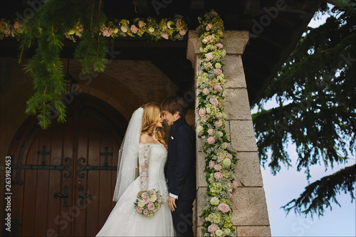 Beautiful couple of young lovers, young blonde bride and handsome stylish groom posing near an ancient church in Switzerland before the wedding ceremony photo