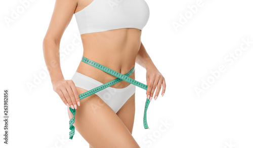 Woman measures waist with tape, slim female belly close-up. Dieting and measuring