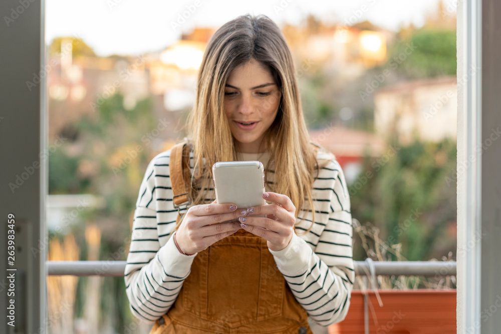 Portrait of young woman standing on balcony looking at cell phone