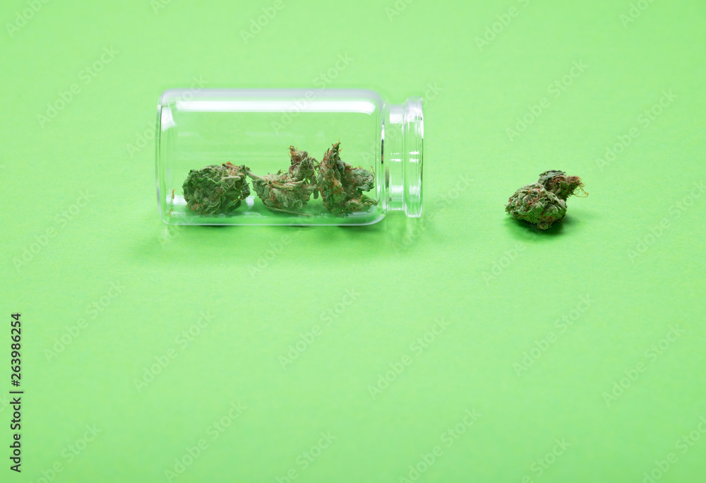 Dried medical cannabis buds in a glass bottle on green background. Dried medical cannabis buds in a glass bottle on green background.