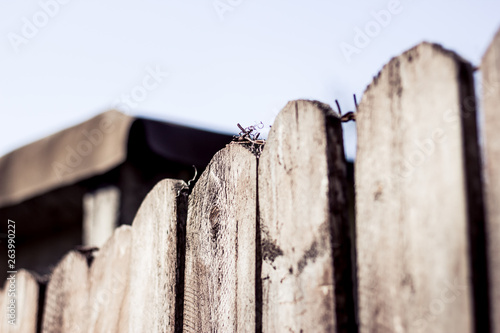 Perspective view of wooden planks and steel cable line with a blurted barn in the background – Closeup of pointy fence with rusty barbed wire on top – Concept background of security and protection photo