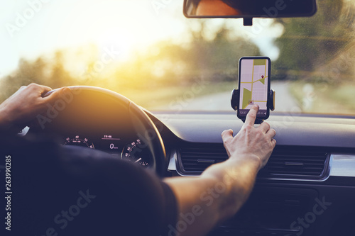 Fototapeta Driver using GPS navigation in mobile phone while driving car at sunset