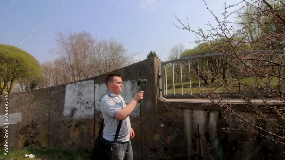 A young man shoots video on a smartphone in spring park. For smooth frames using electronic gimbal. A young man shoots video on a smartphone in spring park. For smooth frames using electronic gimbal.