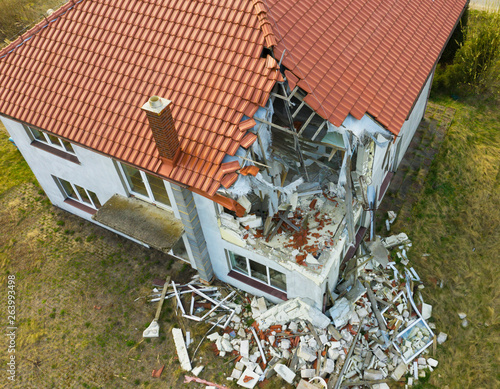 Aerial view on damaged red single house roof after strong wind or explosion. Hole in the rooftop and floor. Rubble on the ground