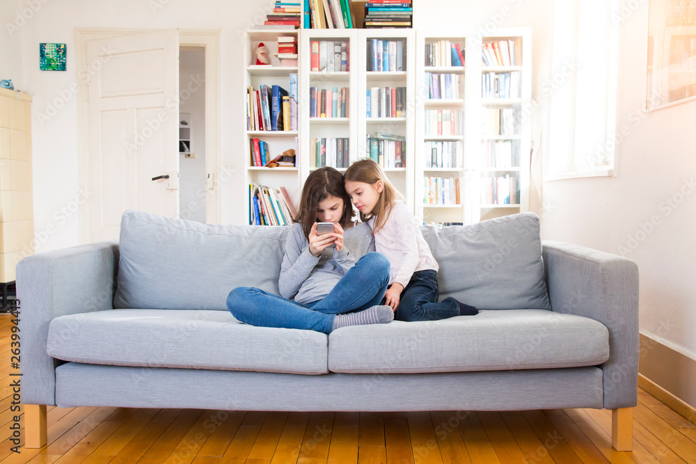 Sisters sitting on couch, using mobile phone Sisters sitting on couch, using mobile phone