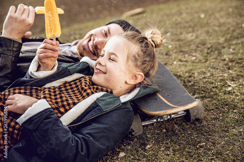 Father and daughter resting on skateboard, eating ice cream