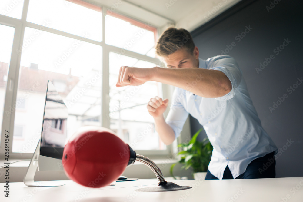 Young businessman at desk in office boxing with punching ball Young businessman at desk in office boxing with punching ball