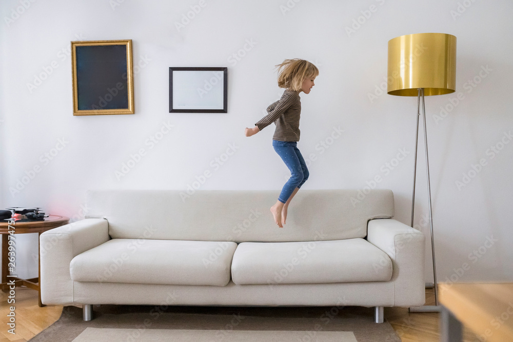 Little girl jumping in the air on the couch at home foto de Stock