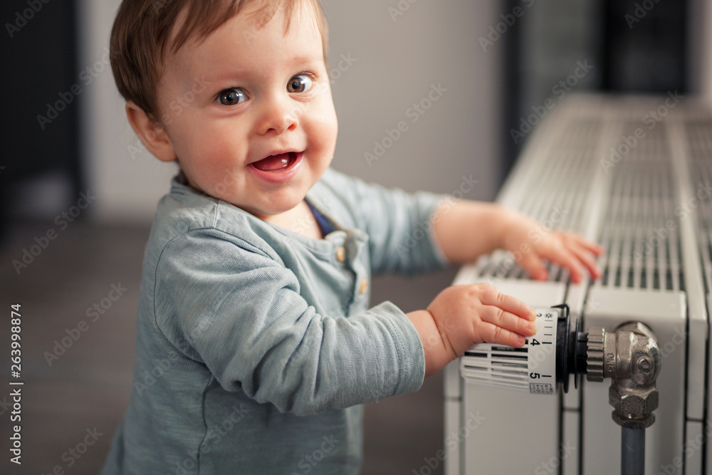 Portrait of smiling baby boy playing with thermostat of heater Stock Photo