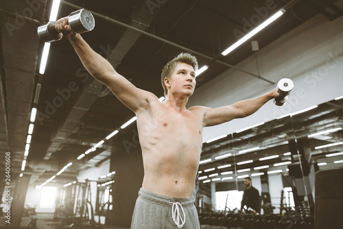 Portrait of athletic man exercising with dumbbells in gym. Athlete man exercises with training dumbbells at biceps brachii muscles in fitness gym