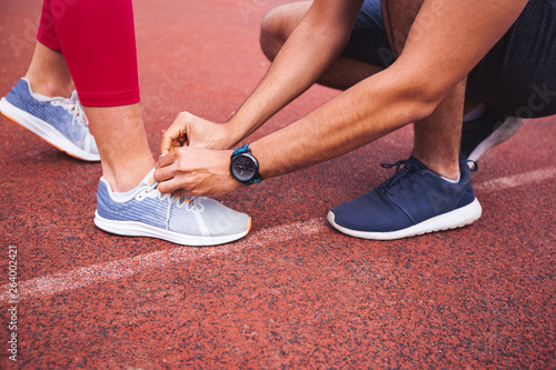 Male runner helping woman to tie running shoes