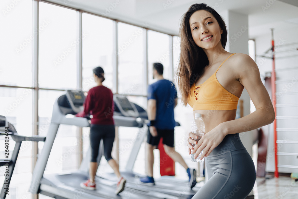 Fototapeta premium young attractive girl in the gym drinking water on the background of treadmills