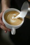 man barista holding a cup of coffee in his hand, pouring a milk, latte art swan on black background