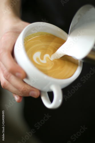 man barista holding a cup of coffee in his hand, pouring a milk, latte art swan on black background