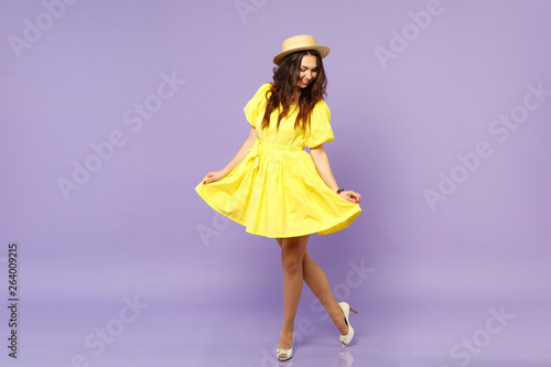 Foto Pretty smiling young woman in yellow dress summer hat looking down, holding skirt isolated on pastel violet wall background in studio