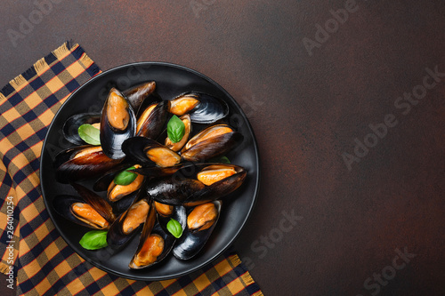 Seafood mussels in a black plate with basil leaves on towel and rusty background