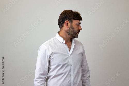 Fashion portrait of handsome young man with brown hair looking relieved, facing forwards and looking at the side. Isolated on white background.