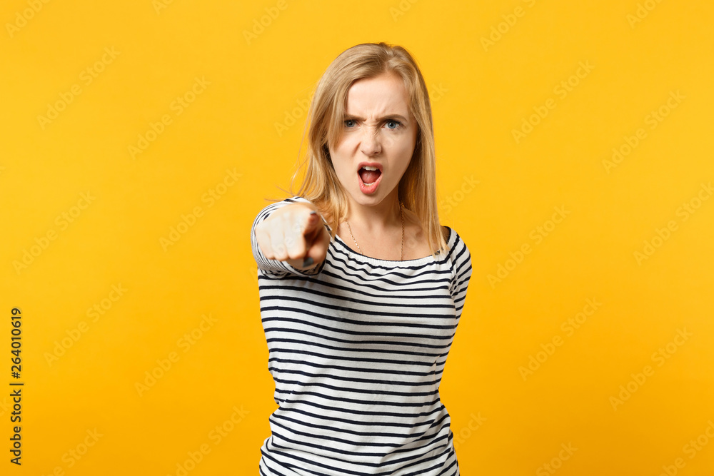 Angry young woman in striped clothes pointing index finger on camera, screaming swearing isolated on yellow orange background in studio. People sincere emotions lifestyle concept. Mock up copy space. Angry young woman in striped clothes pointing index finger on camera, screaming swearing isolated on yellow orange background in studio. People sincere emotions lifestyle concept. Mock up copy space.