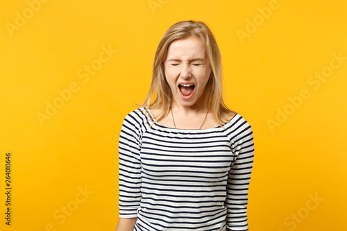 Portrait of crazy young woman in striped clothes keeping eyes closed and screaming isolated on yellow orange wall background in studio. People sincere emotions, lifestyle concept. Mock up copy space.