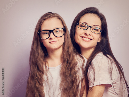 Happy young casual mother and smiling kid in fashion glasses hugging on purple background