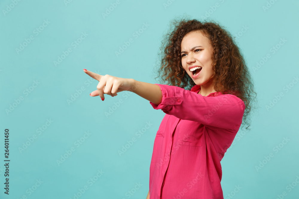 Portrait of perplexed african girl in casual clothes swearing, pointing index finger aside isolated on blue turquoise wall background. People sincere emotions, lifestyle concept. Mock up copy space. Portrait of perplexed african girl in casual clothes swearing, pointing index finger aside isolated on blue turquoise wall background. People sincere emotions, lifestyle concept. Mock up copy space.