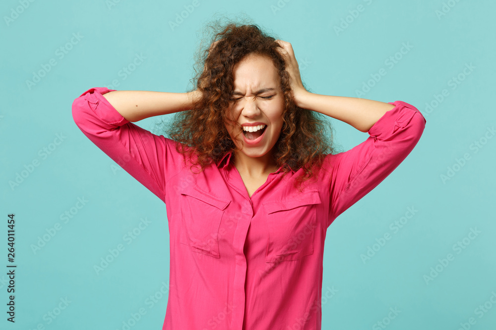 Screaming african girl in casual clothes keeping eyes closed, putting hands on head isolated on blue turquoise background in studio. People sincere emotions, lifestyle concept. Mock up copy space. Screaming african girl in casual clothes keeping eyes closed, putting hands on head isolated on blue turquoise background in studio. People sincere emotions, lifestyle concept. Mock up copy space.