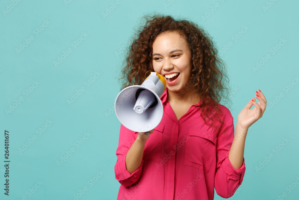 Portrait of laughing funny african girl in pink casual clothes scream in megaphone isolated on blue turquoise wall background in studio. People sincere emotions lifestyle concept. Mock up copy space. Portrait of laughing funny african girl in pink casual clothes scream in megaphone isolated on blue turquoise wall background in studio. People sincere emotions lifestyle concept. Mock up copy space.