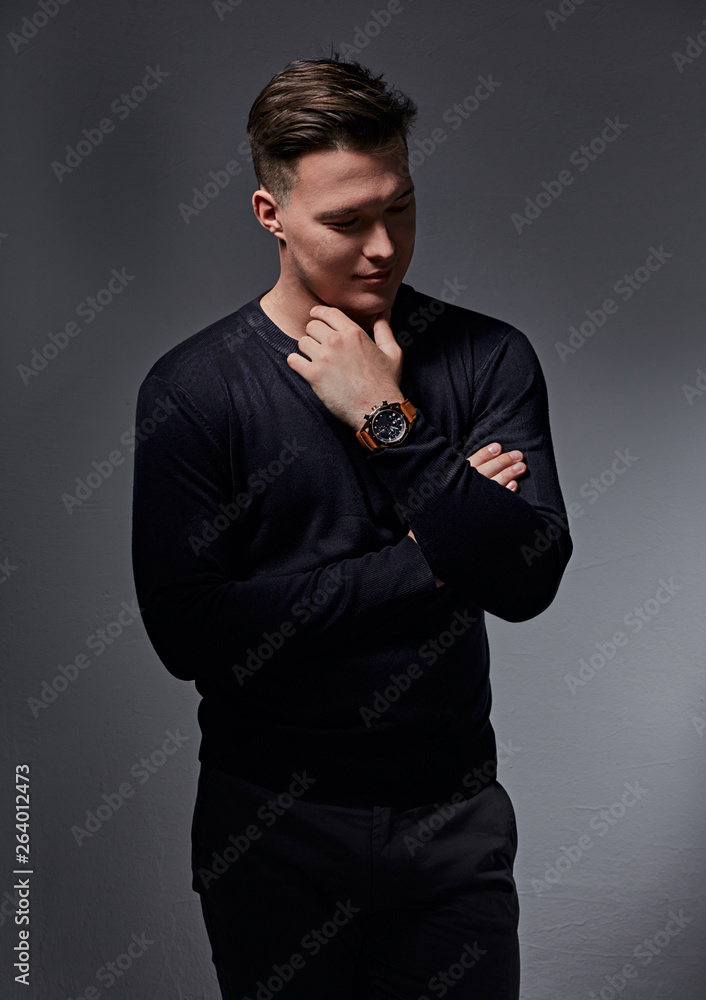 Confident thinking brutal man posing in blue pullover with fashion watch on the hand on dark shadow background. Closeup