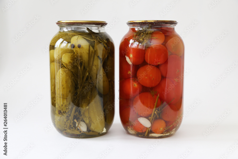 two glass jars with tomatoes and cucumbers closed with a metal lid on light background two glass jars with tomatoes and cucumbers closed with a metal lid on light background