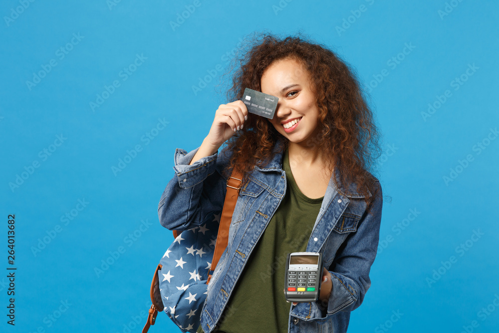 Young african american girl teen student in denim clothes, backpack hold credit card isolated on blue background studio portrait. Education in high school university college concept Mock up copy space Young african american girl teen student in denim clothes, backpack hold credit card isolated on blue background studio portrait. Education in high school university college concept Mock up copy space
