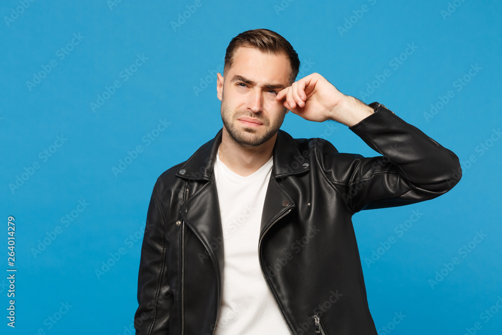 Young sad frustrated worried unshaven man in black jacket white t-shirt looking camera isolated on blue wall background studio portrait. People sincere emotions lifestyle concept. Mock up copy space. Young sad frustrated worried unshaven man in black jacket white t-shirt looking camera isolated on blue wall background studio portrait. People sincere emotions lifestyle concept. Mock up copy space.