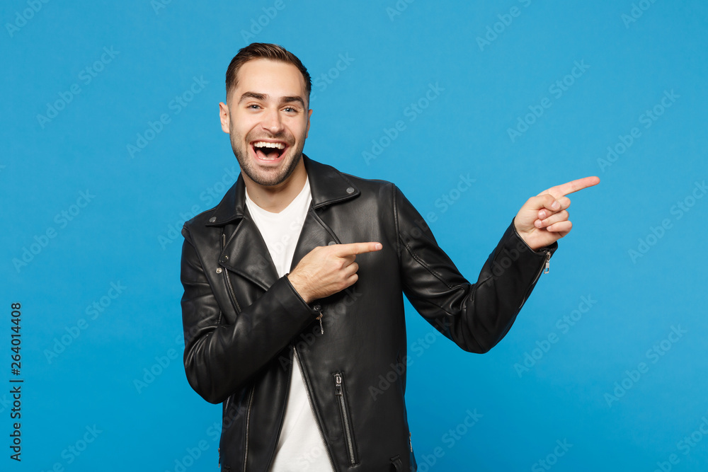 Handsome stylish young unshaven man in black jacket white t-shirt showing on workspace isolated on blue wall background studio portrait. People sincere emotions lifestyle concept. Mock up copy space. Handsome stylish young unshaven man in black jacket white t-shirt showing on workspace isolated on blue wall background studio portrait. People sincere emotions lifestyle concept. Mock up copy space.