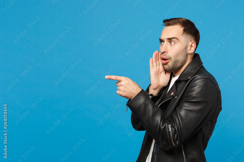 Handsome stylish young unshaven man in black jacket white t-shirt showing on workspace isolated on blue wall background studio portrait. People sincere emotions lifestyle concept. Mock up copy space. Handsome stylish young unshaven man in black jacket white t-shirt showing on workspace isolated on blue wall background studio portrait. People sincere emotions lifestyle concept. Mock up copy space.