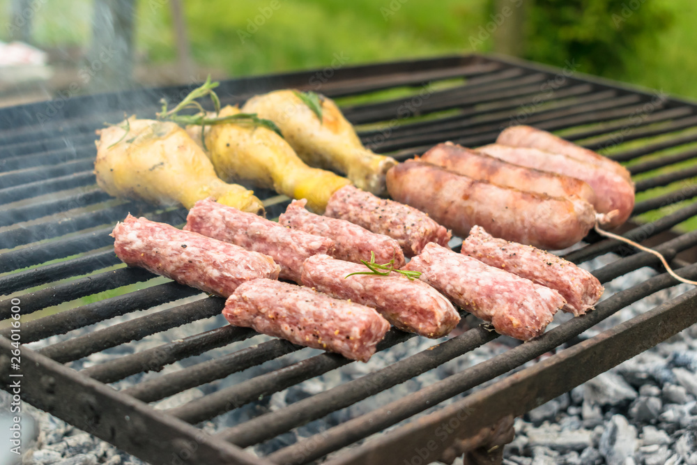 Tasty meat being barbecued on a rustic embers grill in a garden. Chicken with herbs and sausages.