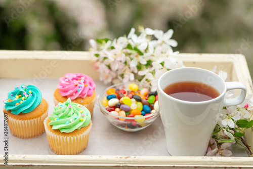 Bright cakes. Cupcakes with colored candies and a cup of coffee or tea on a tray with a bright color background, a sunny morning and a bright mood. spring background