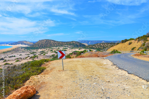 Beautiful view of an amazing bay in Karpas Peninsula, Turkish Northern Cyprus taken on a sunny day from adjacent scenic road. The remote bay is surrounded by small hills with green bushes. 