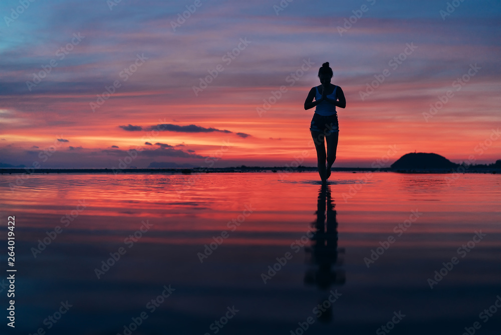 Woman meditating in calm yoga pose on sunset sea beach