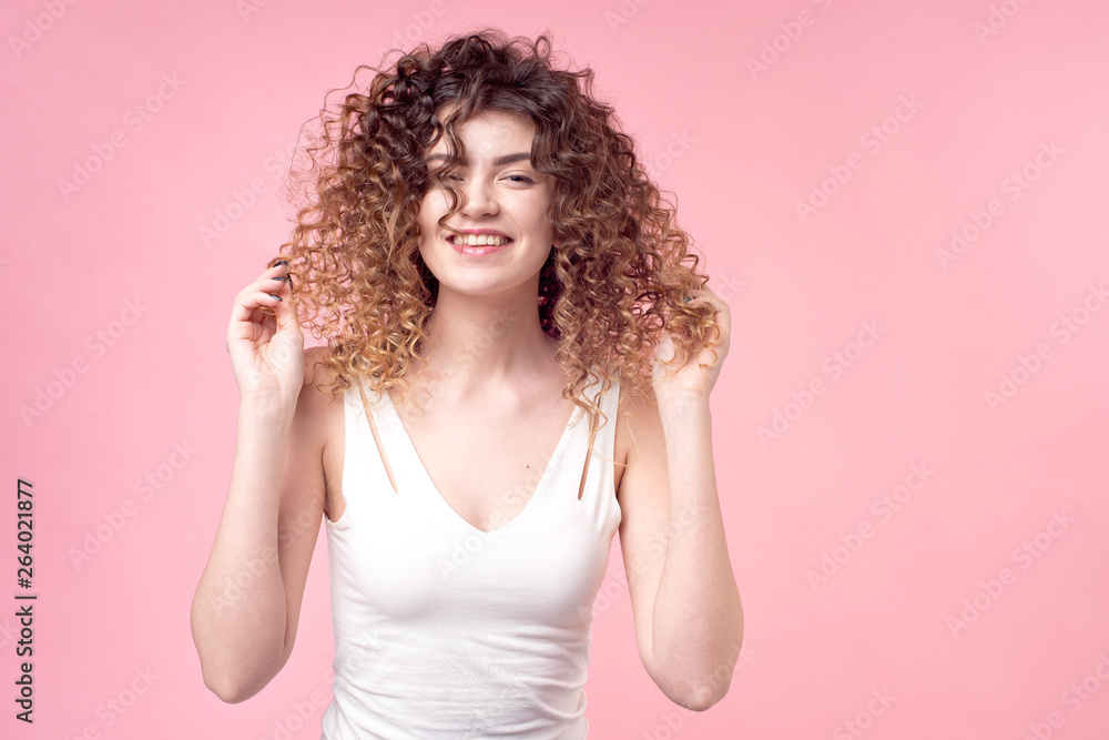 Beautiful woman with a smile on her face with amazing curls in a white T-shirt deloet laying of the hand holds accessories and styling hair curling. Beautiful woman with a smile on her face with amazing curls in a white T-shirt deloet laying of the hand holds accessories and styling hair curling.
