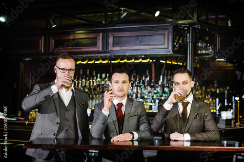 three successful stylish businessmen rest in a pub after work. Colleagues discuss bar work