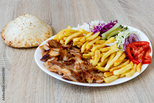 Chiken Doner Kebab on the plate with bread, french fries, tomatoes, onion, pickles and salad on a wooden background. Grilled chicken meat with vegetables.