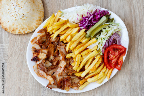 Chiken Doner Kebab on the plate with bread, french fries, tomatoes, onion, pickles and salad on a wooden background. Grilled chicken meat with vegetables.