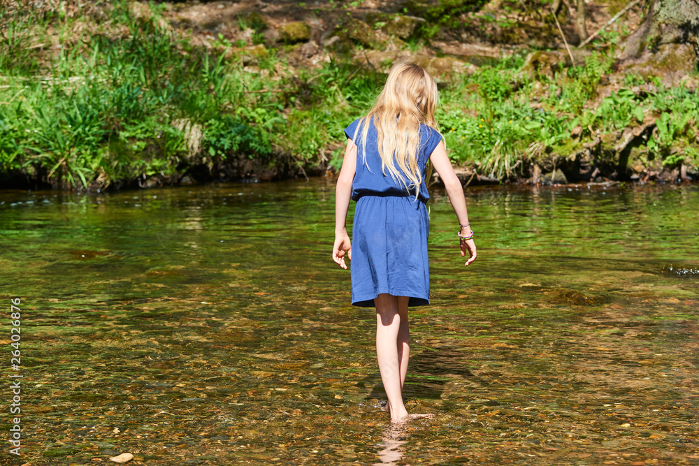 Child cute blond girl playing in the creek. Girl walking in forest stream, looking for pebbles and exploring nature. Summer children fun. Children summer activities Child cute blond girl playing in the creek. Girl walking in forest stream, looking for pebbles and exploring nature. Summer children fun. Children summer activities