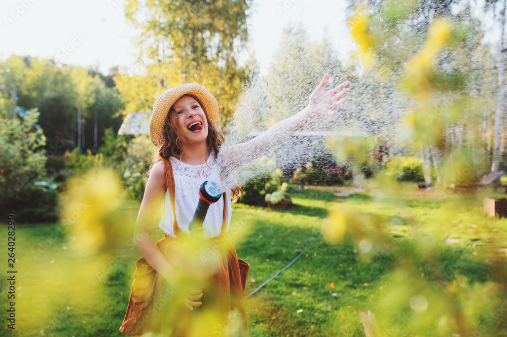 Φωτογραφία happy child girl watering flowers with hose in summer garden, holding water spri