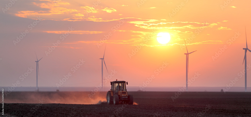 Tractor in field and windmillsin sunrise or sunset