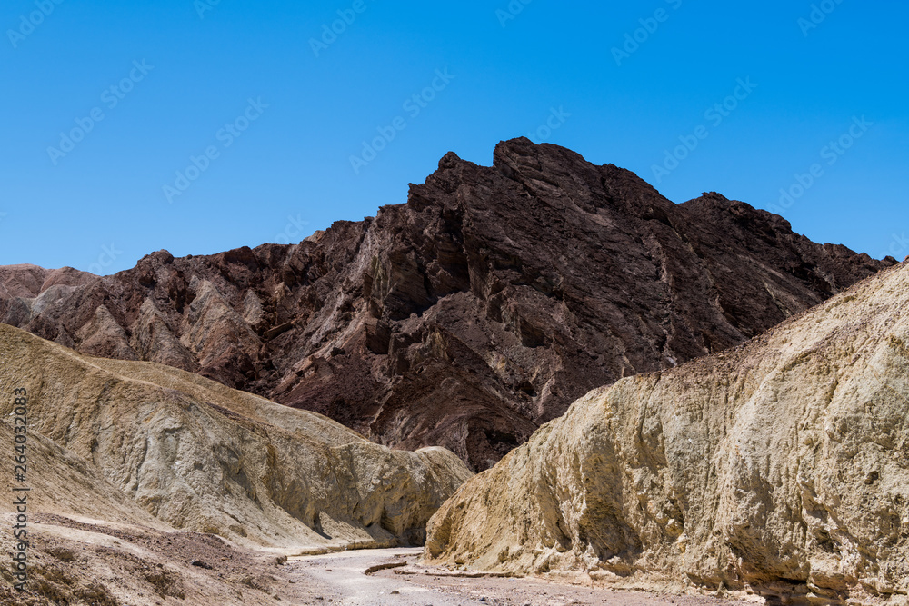 A dry riverbed cuts a pathway through a colorful desert canyon landscape to a rugged mountain peak - the Golden Canyon Trail in Death Valley National Park
