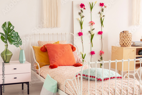 White single metal bed with colorful pillows and doted bedding in chic boho bedroom interior